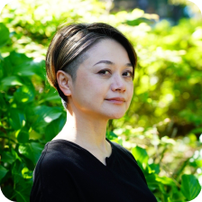 緑の背景で微笑む四本祐子氏の写真